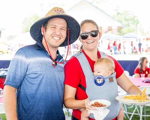 Couple smiling with their baby at tailgate event.