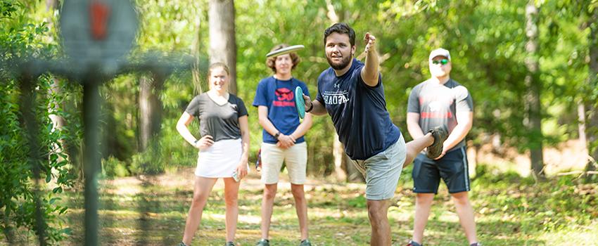 A male student throwing a disc with group of students playing disc golf at USA.